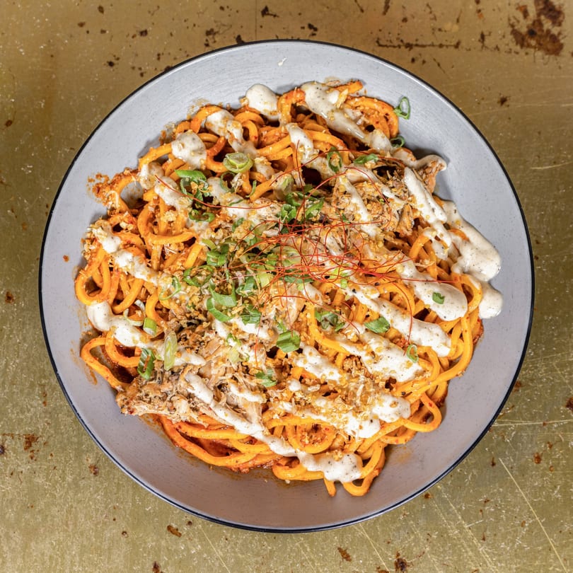 Overhead view of a bowl of orange curly fries drizzled with white sauce, green onions, and spices.