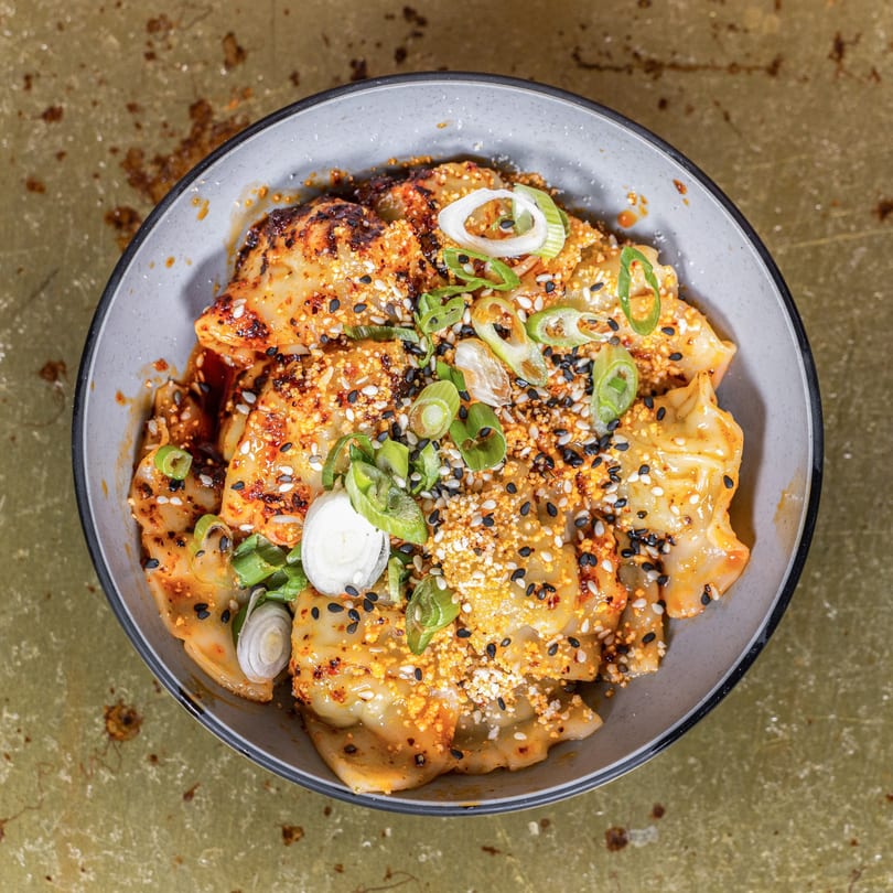 A bowl of dumplings with chili oil, sesame seeds, and sliced green onions.