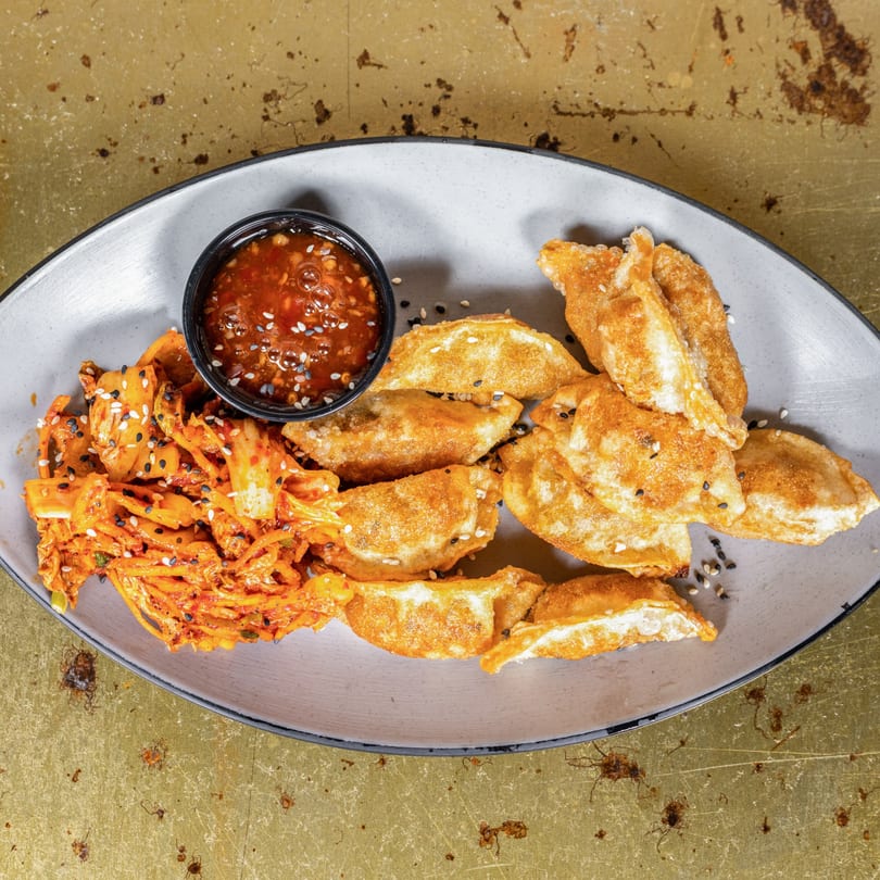 Golden-fried dumplings with kimchi and a dipping sauce, garnished with sesame seeds.